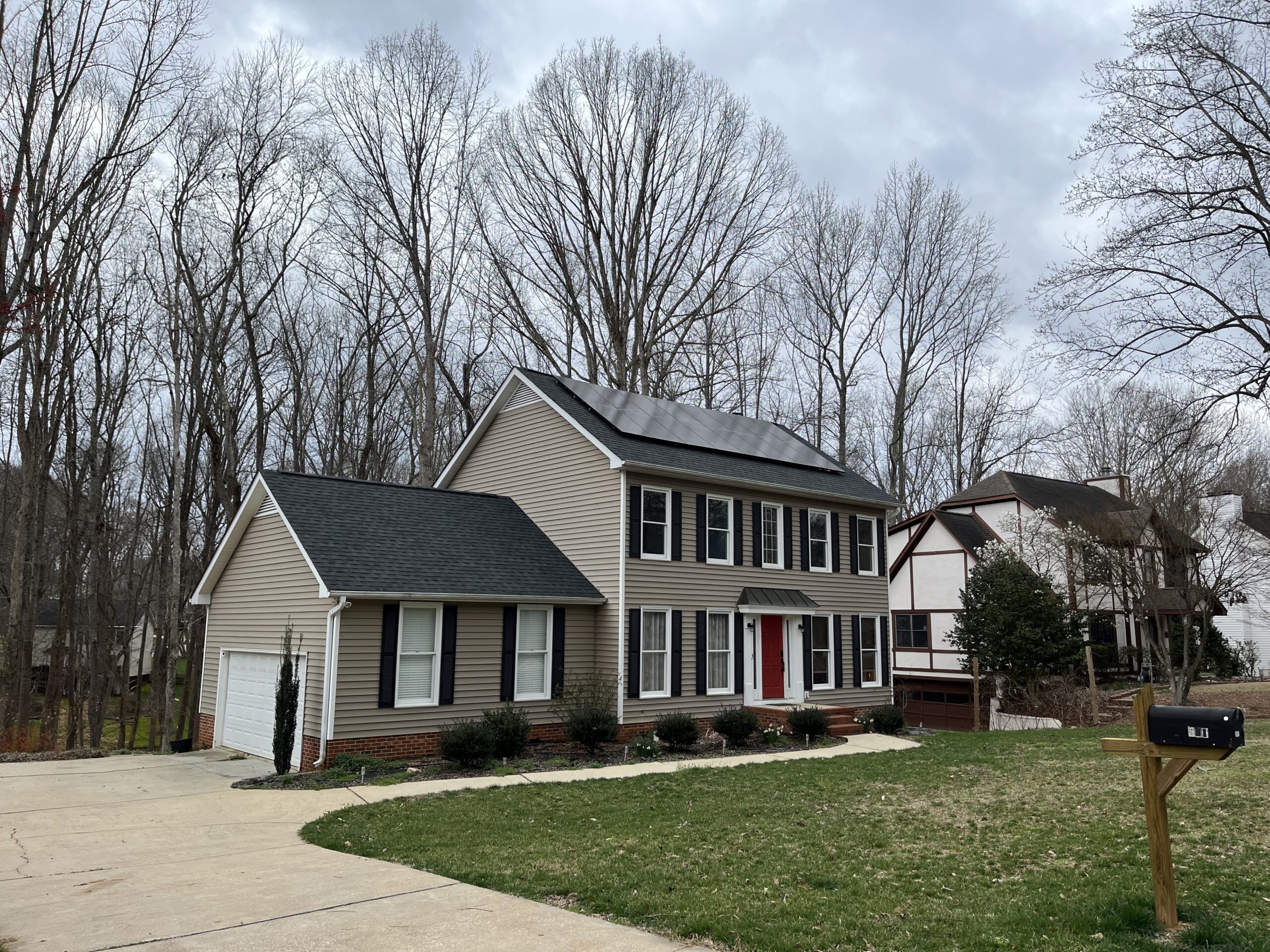 beige suburban house with red door and solar panels on roof